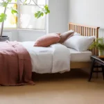 Bright bedroom with a wooden bed, white bedding, pink blanket, and beige carpet.