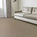 Bright living room with a cream sofa, floor lamp, curtains, and beige textured carpet.