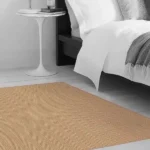 Minimalist bedroom with a beige patterned rug beside a white bed and side table.