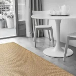Minimalist dining area with a beige woven jute rug and white furniture.