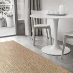 Minimalist dining area with a natural jute rug, white table and chairs, and gray curtains