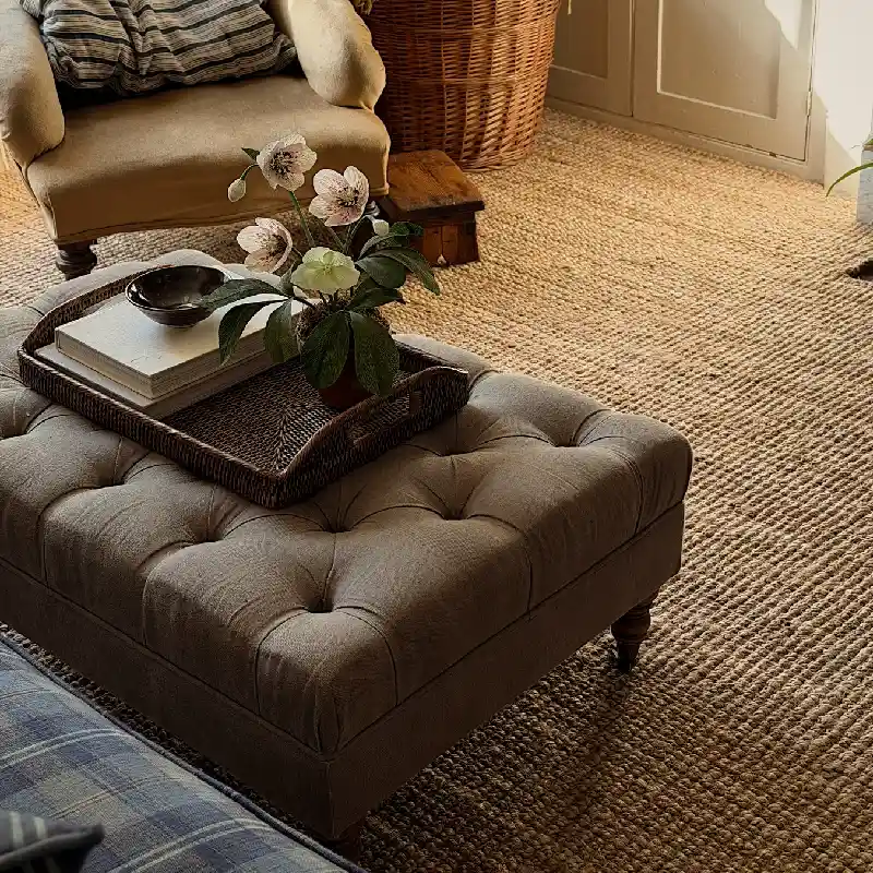Textured natural jute carpet flooring extending beneath a tufted ottoman